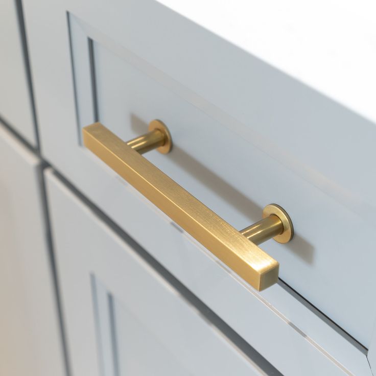 a close up of a drawer handle on a white cabinet with gold handles and knobs