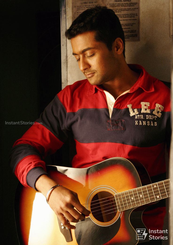 a man is holding an acoustic guitar and looking down at the strings on his left hand