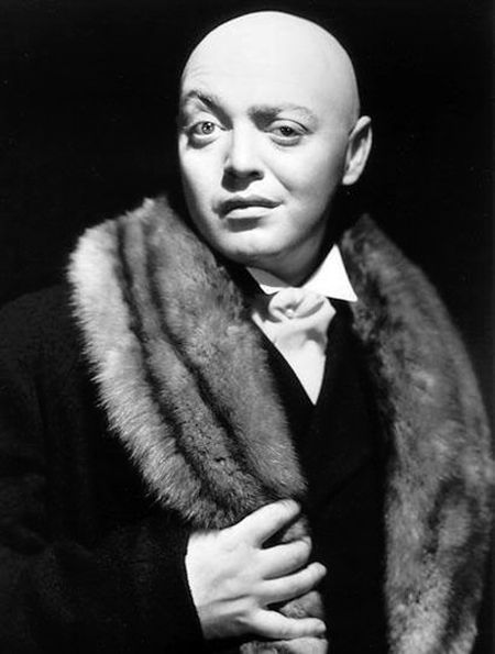 an old black and white photo of a bald man wearing a fur collar with his hands on his chest