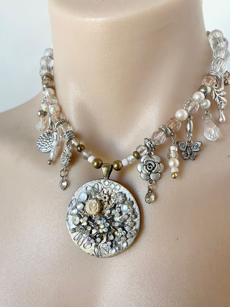 This elaborate beaded charm pendant necklace is the perfect necklace for that special event. It's in shades of white, cream, clear, silver, bronze and gold. The neckline include sourced vintage and retro elements. It comes together with a collage pendant as the main feature. This would be a beautiful stunner accessory for that special dress and attire. This handmade piece is made and ready to be shipped. All my wearable works are delivered to you without any packaged receipt so they are perfect White Necklace With Charms And Round Pendant, Handmade White Pearl Charm Necklaces, Unique White Round Necklace, Unique White Round Necklaces, Unique Round White Necklaces, Vintage White Charm Necklaces, White Beaded Pearl Charm Necklaces, Bohemian Wedding Necklaces With Vintage Charm, Bohemian Wedding Necklace With Vintage Charm