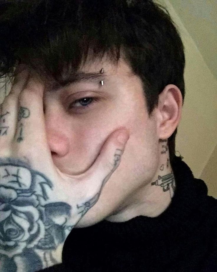 a young man with tattoos covering his face and hand over his mouth, looking at the camera