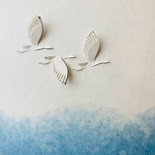 two paper birds flying in the air on top of blue and white watercolor paper