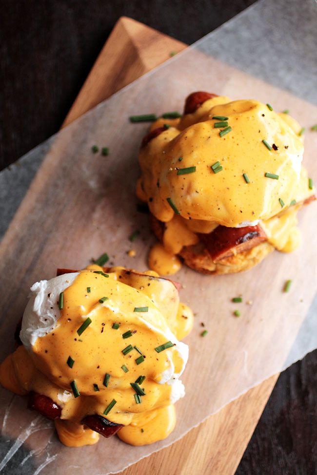 two eggs benedicts are sitting on a cutting board