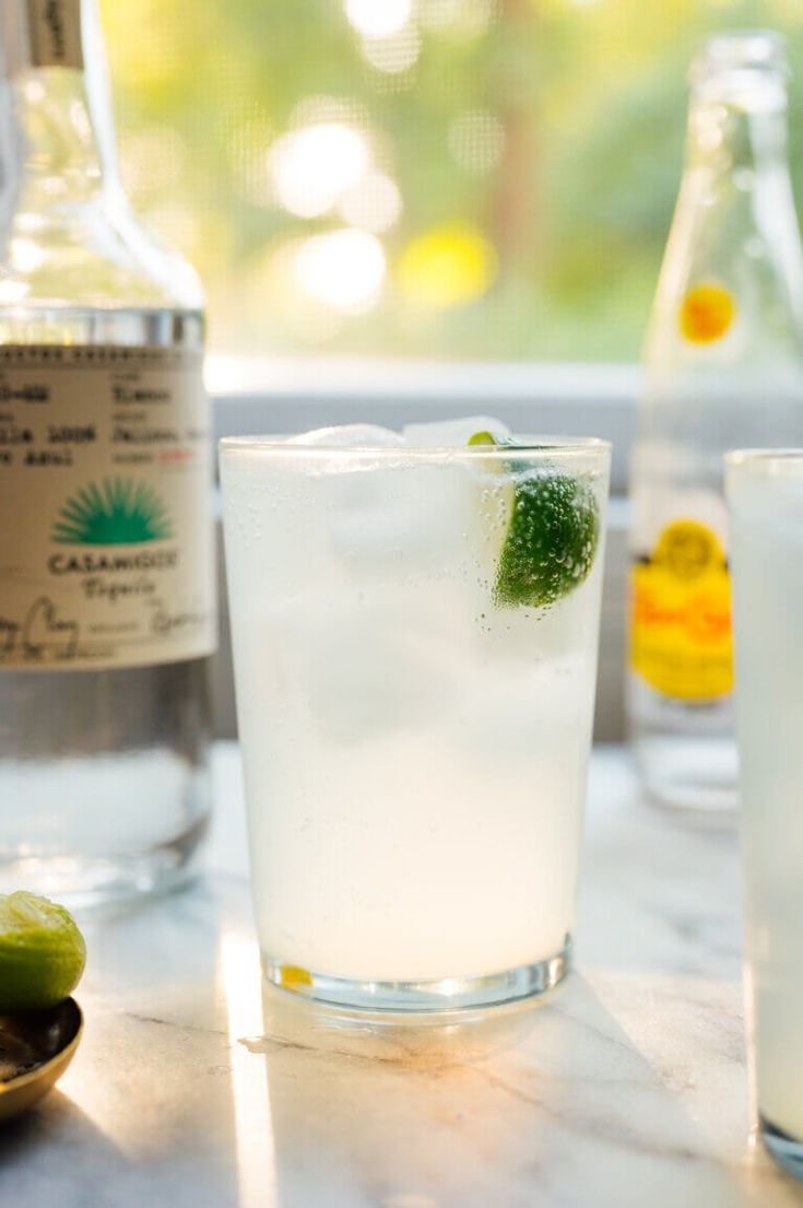 two glasses filled with ice and limes next to bottles