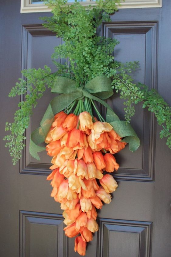 an orange flower hanging on the front door with greenery around it's edges