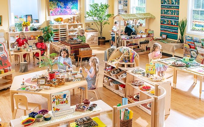 children's playroom with wooden tables and chairs filled with books, toys and other items