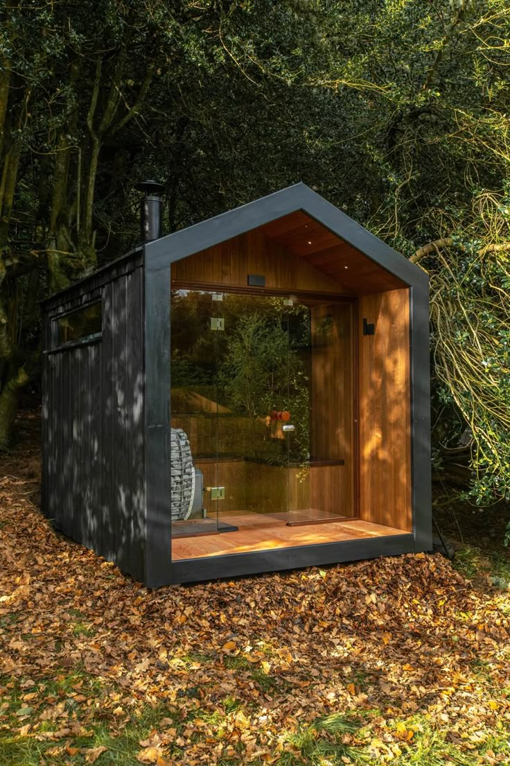 an outdoor sauna in the woods with leaves on the ground and trees around it