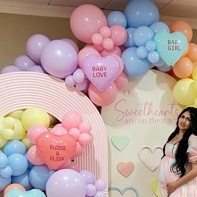 a pregnant woman standing in front of balloons and heart - shaped signs at a baby shower