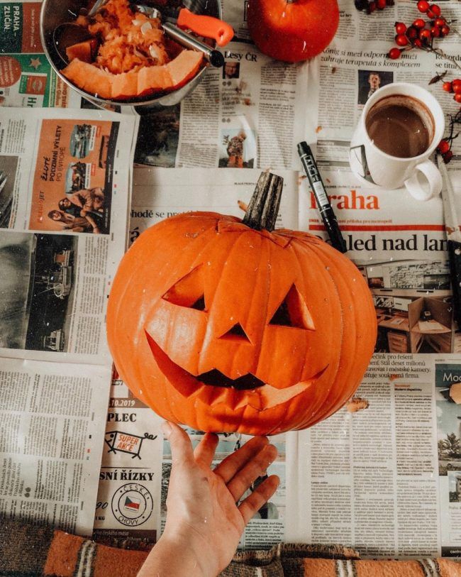 a person holding up a carved pumpkin in front of a newspaper with other items on the table