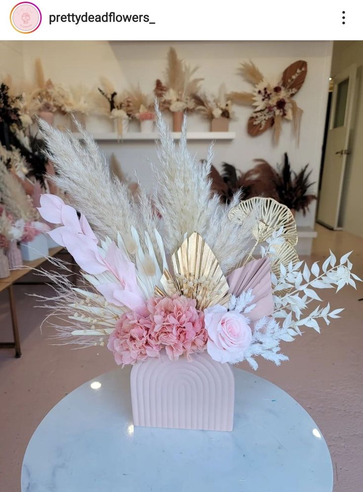 a vase filled with flowers and feathers on top of a white table in a room