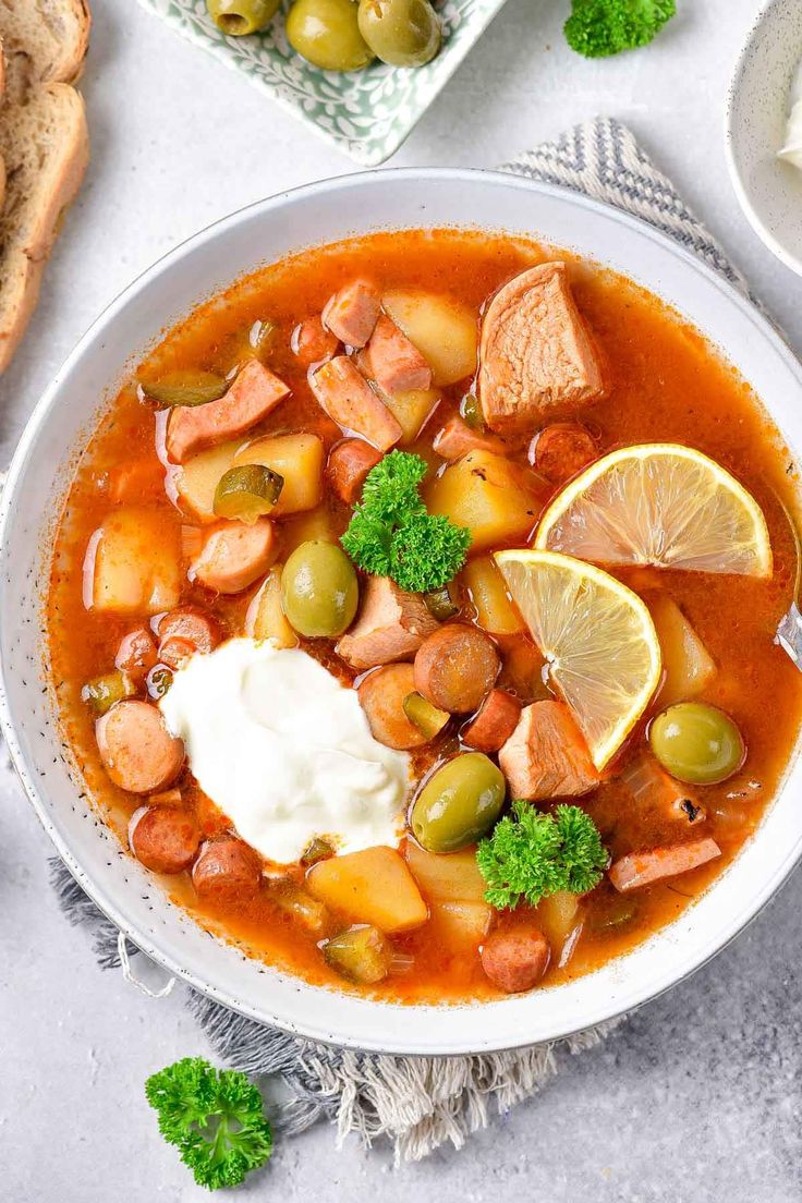 a white bowl filled with soup and vegetables on top of a table next to bread