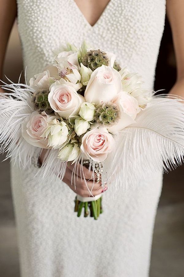 a bridal holding a bouquet of white and pink flowers with feathers on the side