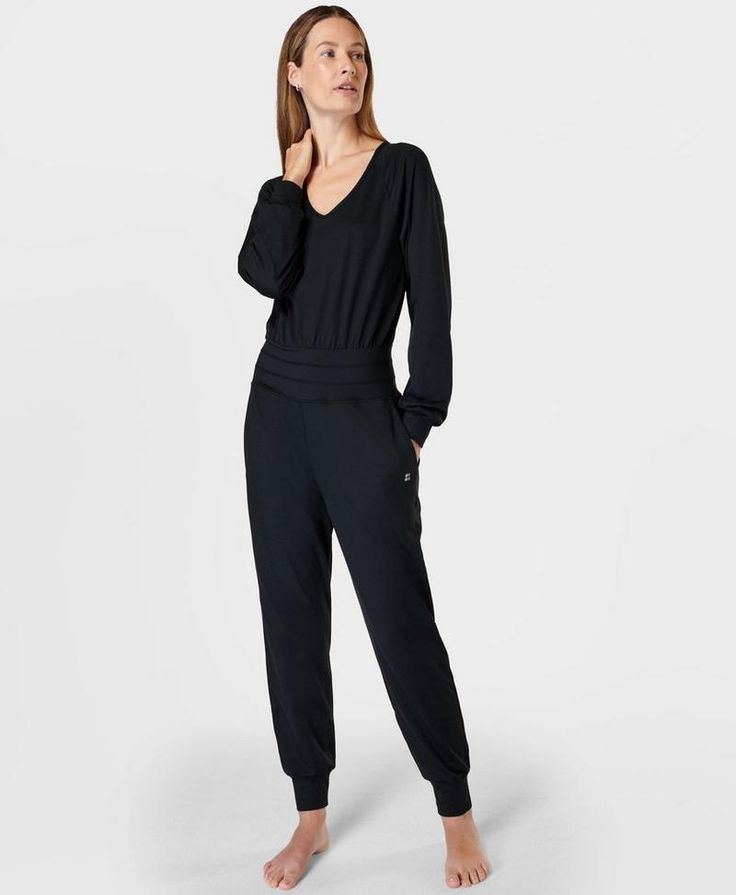 Our new-and-improved jumpsuit for low-impact workouts. Updated 85% recycled fabric is ultra-soft, smooth and sweat-wicking. Loose fit with V-neck and long sleeves. Fitted waistband, cuffs and ankles to stay put as you move. Inseam length: 73cm / 29”. Model wears size S and is 178cm/5'10" tall. Style Code: SB9727Colour: Black Casual Long Sleeve Jumpsuits For Gym, Athleisure Activewear With Elastic Cuffs For Lounging, Sporty V-neck Loungewear Activewear, Sporty V-neck Activewear, Casual Workout Jumpsuits And Rompers With Long Sleeves, Casual Long Sleeve Jumpsuits And Rompers For Workout, Casual Long Sleeve Workout Jumpsuits And Rompers, Relaxed Fit V-neck Athleisure Activewear, Sporty Activewear With Elastic Cuffs For Lounging