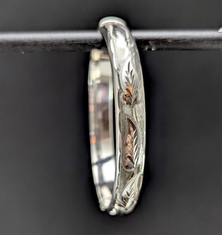 A pretty classic hinged sterling silver bangle bracelet with a leafy engraved design on one side. Inside the bangle has a patent number, a makers mark for Bracelon Ltd and full English silver hallmarks with a date letter for 1981. In good vintage condition. Inner circumference: 17.5 cm Width: 9 mm Weight: 12 grams approx Materials: Sterling silver Postage Our standard UK postage option uses Royal Mail second class post, if you require your order faster then you can upgrade postage options for an Classic Etched Bangle Bracelets, Classic Etched Bangle Bracelet, Classic Etched Bangle Jewelry, Classic Etched Bangle For Wedding, Classic Etched Wedding Bangle, Anniversary White Gold Bangle With Shiny Finish, Classic Engraved Sterling Silver Bangle Bracelet, Classic Etched Bracelet Jewelry, Classic Etched Sterling Silver Bracelet