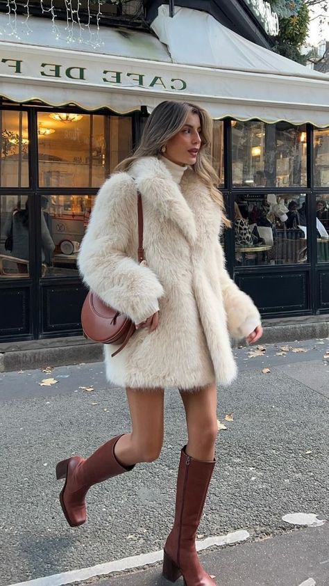 a woman is walking down the street wearing boots and a coat with fur on it