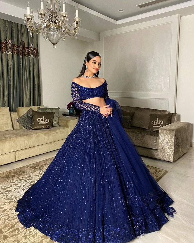 a woman in a blue gown standing in front of a couch and chandelier