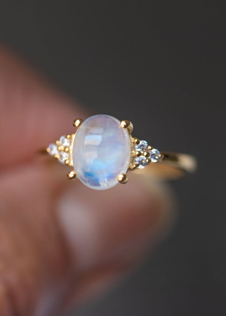 Our Fleur Moonstone ring features a single blue flash Moonstone set in a sturdy four-prong setting surrounded with three white topaz on each side. It can be worn as an engagement ring and a statement ring stacked with our Colline and Hana ring for a unique look. Always handmade with genuine and natural stones on solid sterling silver and thick gold vermeil that will stand the test of time. D E T A I L S * Materials - 18k gold vermeil on solid 925 sterling silver, genuine blue flash Moonstone * G Everyday Oval Moonstone Ring, Dainty Moonstone Ring For Everyday, Everyday Moonstone Birthstone Ring, Minimalist Oval Moonstone Ring For Everyday, Minimalist Moon Shaped Moonstone Ring As Gift, Minimalist Moon-shaped Moonstone Ring As Gift, Minimalist Moon-shaped Moonstone Ring For Gift, Minimalist Moon-shaped Moonstone Ring, Modern Oval Moonstone Promise Ring