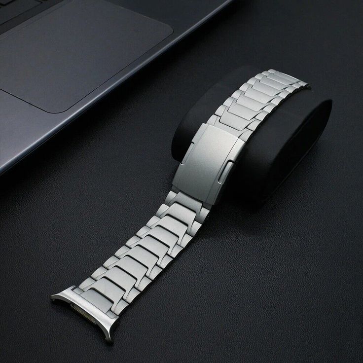 a silver watch sitting on top of a black table next to a laptop computer and keyboard