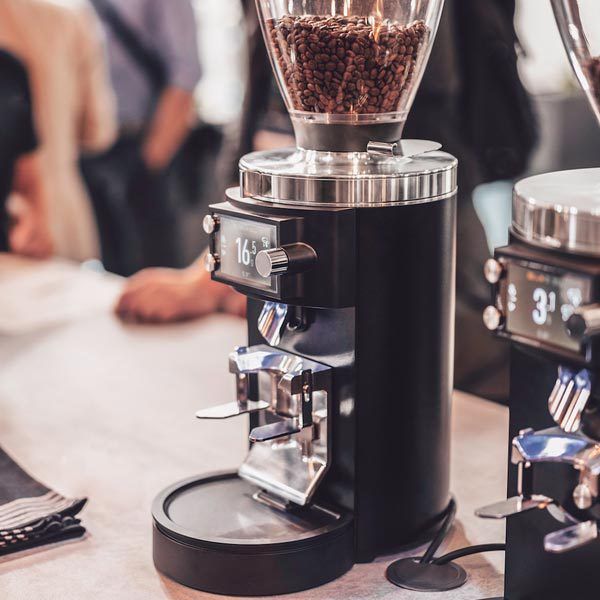 a coffee maker sitting on top of a wooden table next to a couple of people