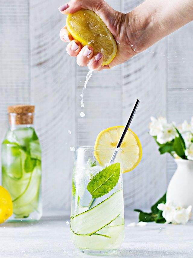 a person pouring water into a glass with lemon slices and mint