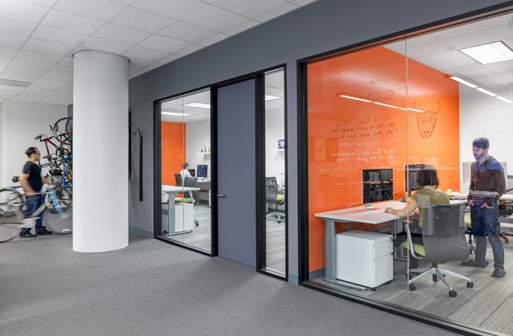 an office with glass walls and people working in the background on computers, laptops, and other electronic equipment