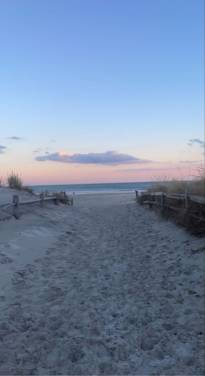 a sandy path leading to the beach at sunset