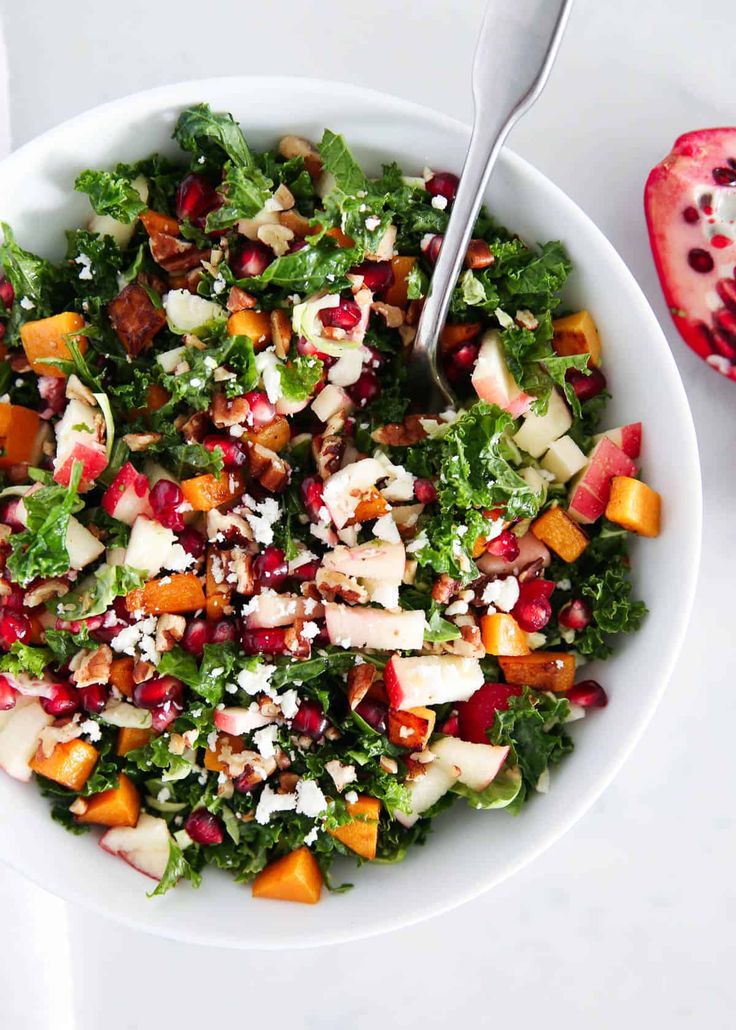 a white bowl filled with salad next to a pomegranate