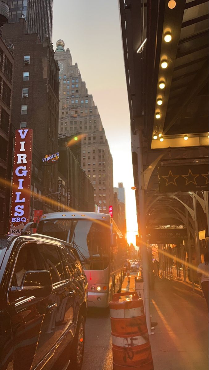 cars parked on the side of a street next to tall buildings and traffic lights at sunset