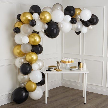 an arch made out of black, white and gold balloons is displayed in the corner of a room