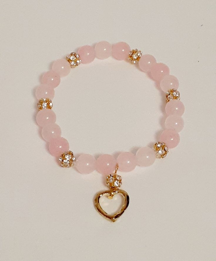 Rose quartz is known as the stone of love and reconcilliation and is customarily used as a gift of love.   It is thought to make one open to love and compassion.  Some believe that rose quartz has calming effects and helps to develope strong friendships. Two styles of bracelets are shown : # 1 - 8mm genuine rose quartz beads  with silver & rhinestone accent bands and an open silver heart charm.  #2- 8 mm genuine rose quartz beads with rose gold & rhinestone accent clusters and an open rose gold heart charm. Rose quartz is typically a cloudy translucent pink colour.  These bracelets are sure to plesse with its delicate colour of pink and silver or gold accents. This stretch rose quartz bracelet is made with natural pink rose quartz stones that have been polished to a glossy finish. It featu Gold And Pink Bracelet, Pink And Gold Bracelet, Pink Jewelry For Meditation, Pink Natural Stones Jewelry For Friendship, Pink Rose Quartz Gemstone Beaded Bracelets, Pink Rose Quartz Gemstone Bracelets, Pink Rose Quartz Bracelets For Meditation, Pink Natural Stone Bracelets For Friendship, Pink Spiritual Charm Bracelet For Friendship