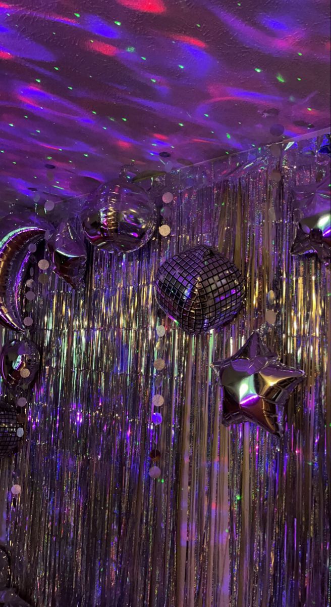 many shiny objects hanging from the ceiling in a room with purple and green lights on it