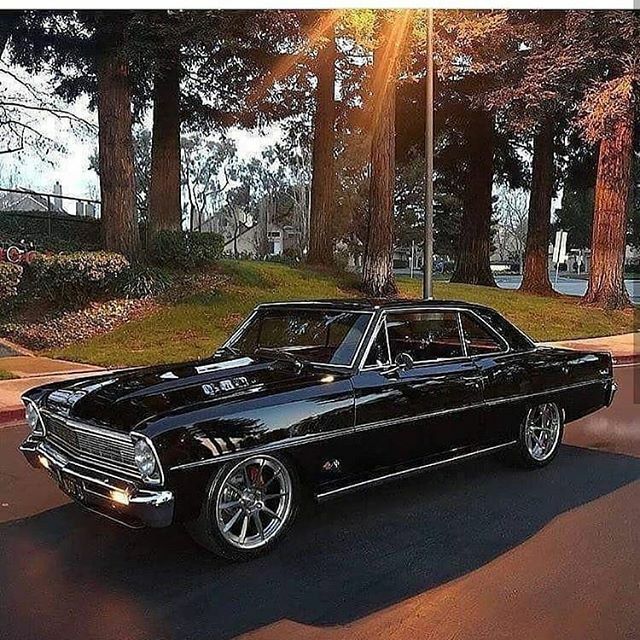 an old black car is parked on the side of the road in front of some trees