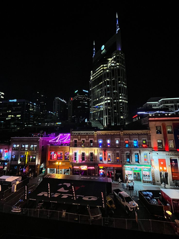 the city is lit up at night with bright lights on buildings and cars parked in front