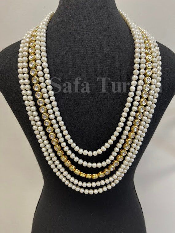 Wearing a pearl necklace as part of the groom's wedding attire can add a touch of sophistication and elegance to the groom's look and can be a meaningful way to incorporate cultural traditions into the wedding celebration. Material: Beads Brooch- Kundan Color: Cremish White Pearls Package Includes: 1 Unique Handmade Groom Necklace Color Disclaimer: Actual colors can differ. This is because every display screen has a different capacity to display colours. So, the color variation might occur becau Gold Jewelry With Pearl Buttons For Wedding, Gold Wedding Jewelry With Pearl Buttons, White Pearl Button Wedding Jewelry, Elegant Gold Pearl Necklace For Marriage, White Wedding Jewelry With Pearl Details, Gold Round Bead Pearl Necklace For Weddings, Gold Round Beads Pearl Necklace For Wedding, Elegant White Pearl Necklace For Ceremonial Occasions, Gold Pearl Necklace With Round Beads For Wedding