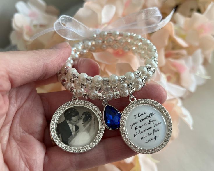 a person holding two bracelets with pictures on them and pearls around the edges, in front of a bouquet of flowers