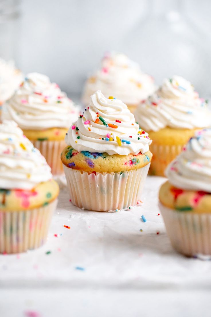 cupcakes with white frosting and sprinkles on wooden table top