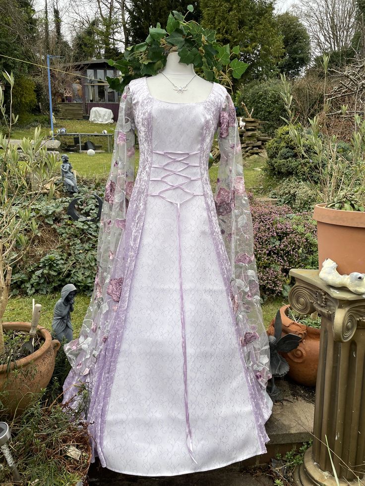 a white and purple dress sitting on top of a wooden table next to potted plants