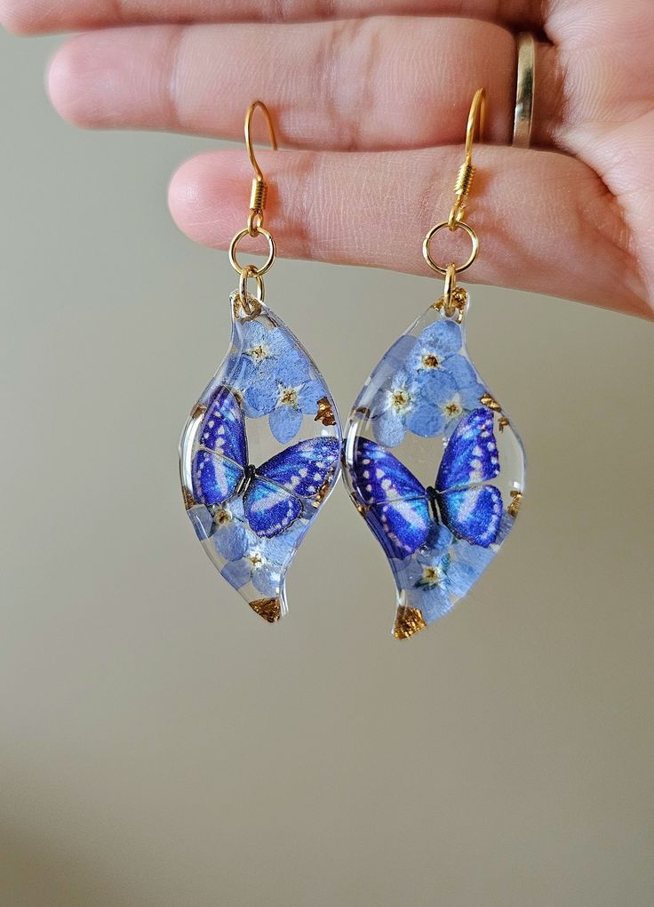 a pair of earrings with blue and gold butterflies hanging from it's ear wires