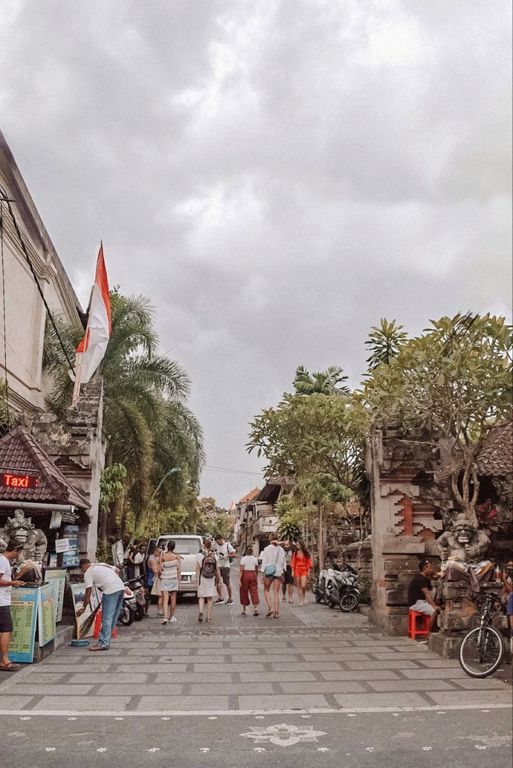 people are walking down the street in front of shops and parked cars with flags on them