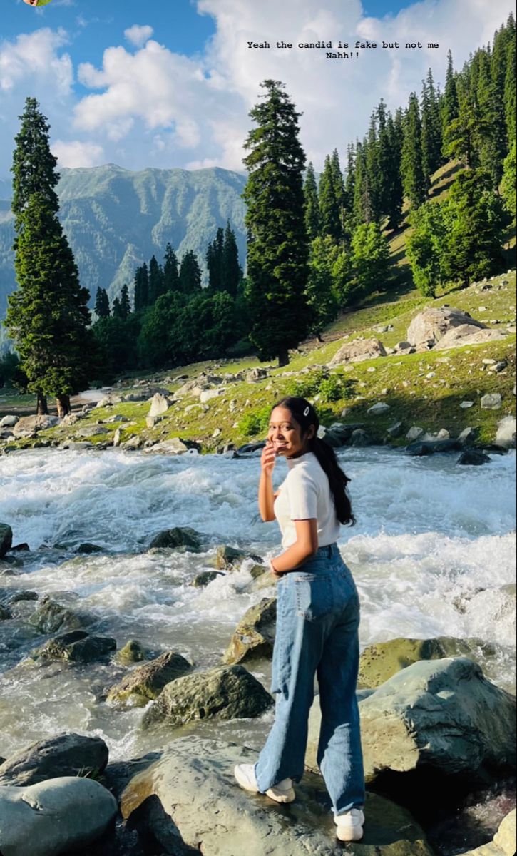 a woman standing on top of a rock next to a river