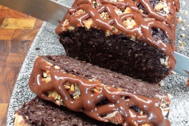 a loaf of chocolate cake with nuts on top and a knife in the middle cutting it