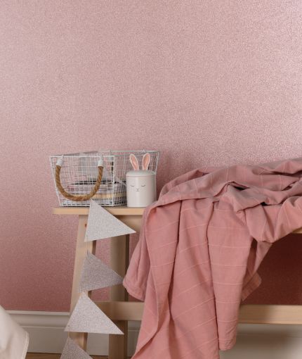 a bed with pink sheets and blankets on it next to a wooden table in front of a pink wall