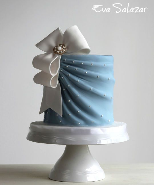 a blue and white decorated cake on top of a stand with pearls in the middle