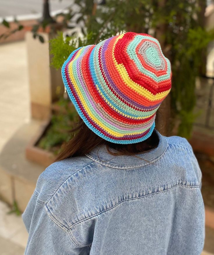 a woman wearing a multicolored knitted hat and denim jacket looking at the street