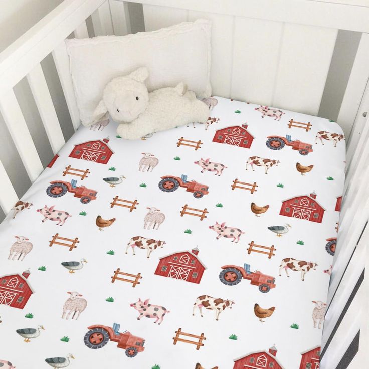 a white crib bed with farm animals and barnyards printed on it, next to a stuffed animal