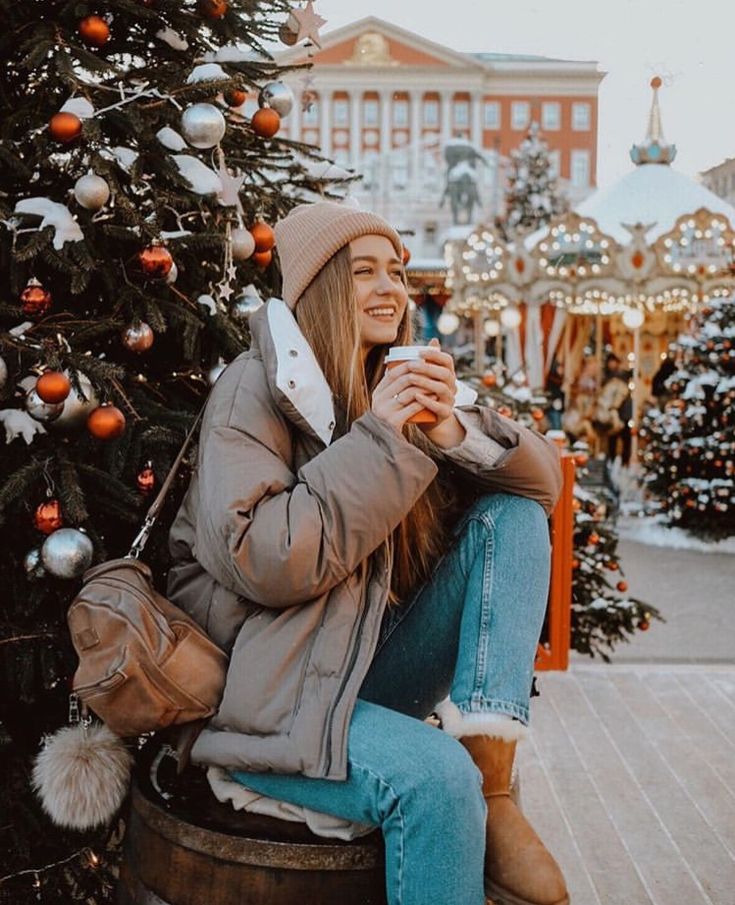 a woman sitting on top of a barrel next to a christmas tree holding a cup