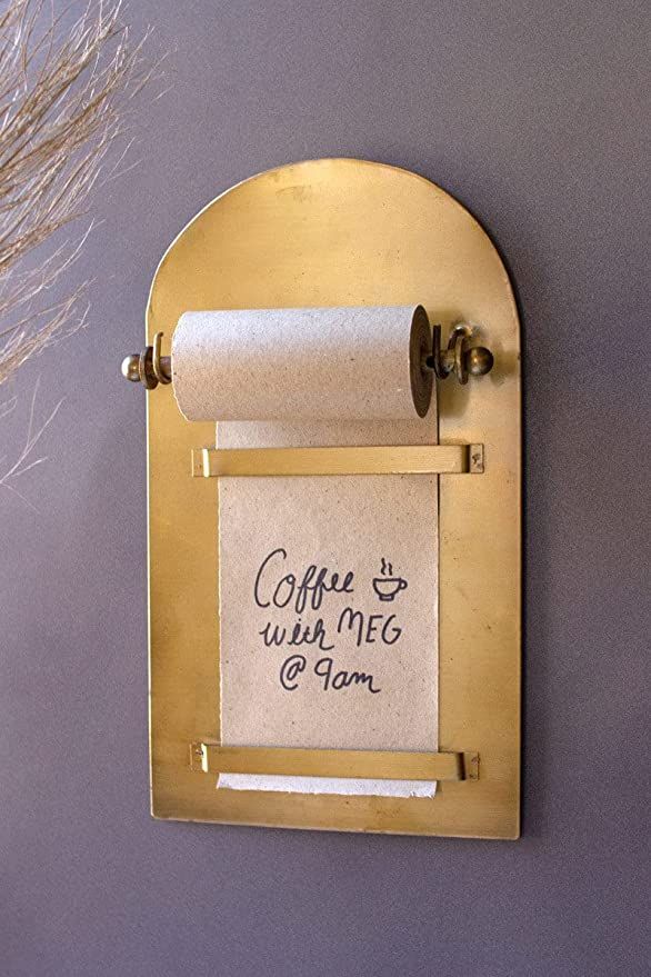 a gold toilet paper holder with a note attached to the wall next to a roll of toilet paper