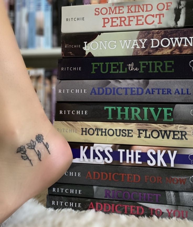 a stack of books with tattoos on their ankles and feet sitting next to each other in front of a book shelf