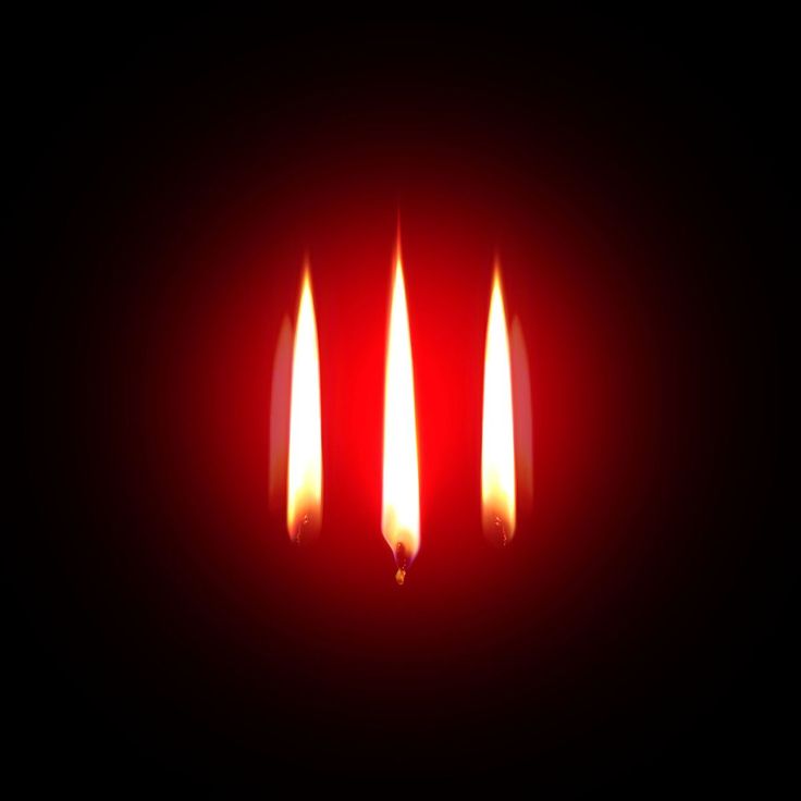 three lit candles in the dark on a red background