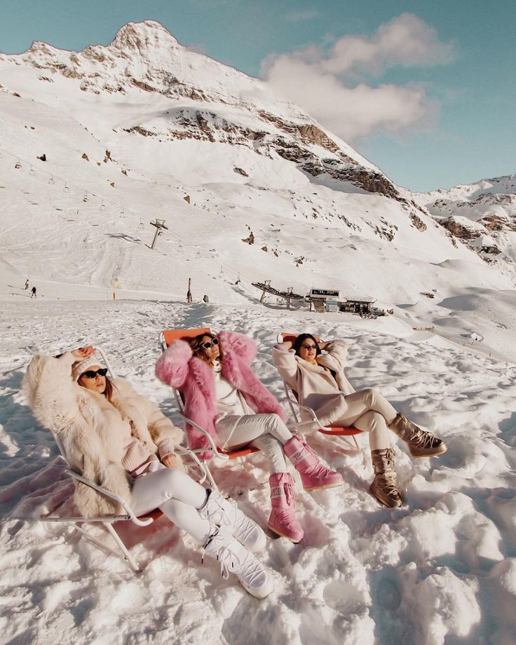 three women sitting in the snow with skis on their feet and one wearing sunglasses